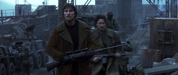 Movie still from “Reign of Fire” (2002), directed by Rob Bowman – A man holding a gun while standing next to another man; Medium shot, Over the shoulder angle