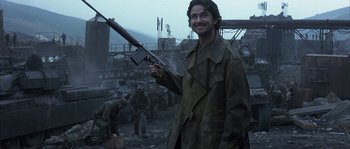 Movie still from “Reign of Fire” (2002), directed by Rob Bowman – A man holding a rifle in a war zone; Medium shot, Low angle