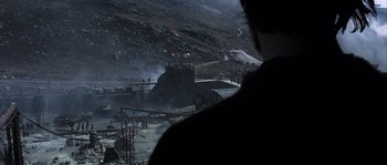 Movie still from “Reign of Fire” (2002), directed by Rob Bowman – A man standing in front of a building on a hill; Extreme Wide shot, Over the shoulder angle