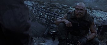 Movie still from “Reign of Fire” (2002), directed by Rob Bowman – A man sitting on the ground with a gun in his hand; Medium shot, Over the shoulder angle