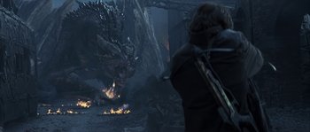 Movie still from “Reign of Fire” (2002), directed by Rob Bowman – A man standing in front of a fire and a dragon; Wide shot, Over the shoulder angle