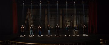 Movie still from “Rent” (2005), directed by Chris Columbus – A group of people standing on a stage in front of lights; Wide shot, High angle