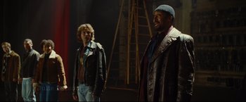 Movie still from “Rent” (2005), directed by Chris Columbus – Two men standing next to each other in a dark room; Medium shot, Over the shoulder angle