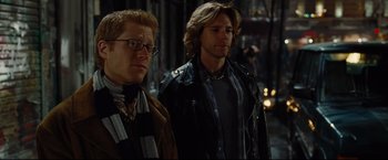 Movie still from “Rent” (2005), directed by Chris Columbus – A couple of men standing next to each other on a street; Medium shot, Over the shoulder angle