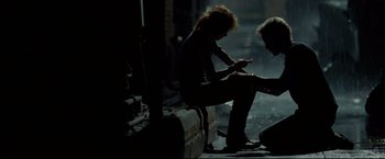 Movie still from “Rent” (2005), directed by Chris Columbus – Two people sitting on a bench looking at a phone; Wide shot, Low angle
