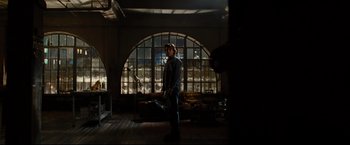 Movie still from “Rent” (2005), directed by Chris Columbus – A man standing in a room in front of an arched window; Wide shot, Low angle
