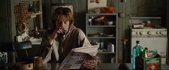 Movie still from “Rent” (2005), directed by Chris Columbus – A person sitting at a table reading a newspaper; Medium shot, Over the shoulder angle
