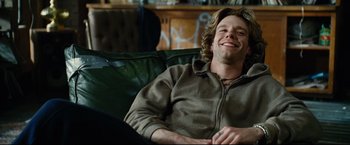 Movie still from “Rent” (2005), directed by Chris Columbus – A man sitting on a couch smiling for the camera; Close Up shot, Low angle