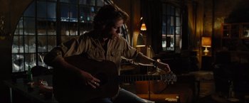 Movie still from “Rent” (2005), directed by Chris Columbus – A man sitting on the ground playing a guitar; Medium shot, Over the shoulder angle