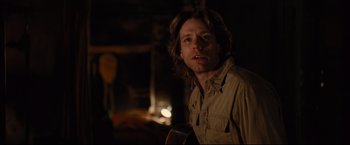 Movie still from “Rent” (2005), directed by Chris Columbus – A man with long brown hair is holding a guitar in front of a fireplace; Close Up shot, Over the shoulder angle