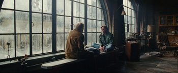 Movie still from “Rent” (2005), directed by Chris Columbus – Two men sitting in front of a large window; Wide shot, Over the shoulder angle