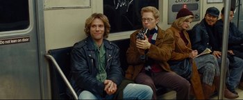Movie still from “Rent” (2005), directed by Chris Columbus – Two young men sitting on a train looking at a camera; Medium shot, Over the shoulder angle