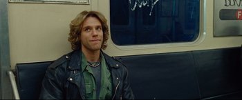 Movie still from “Rent” (2005), directed by Chris Columbus – A man sitting on a train looking at the camera; Close Up shot, Over the shoulder angle