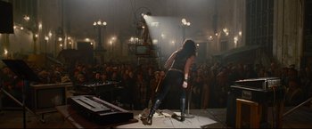 Movie still from “Rent” (2005), directed by Chris Columbus – A person on a stage with a microphone; Wide shot, High angle