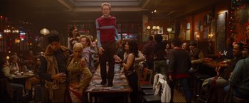 Movie still from “Rent” (2005), directed by Chris Columbus – A man standing on top of a table in front of a group of people; Wide shot, Low angle