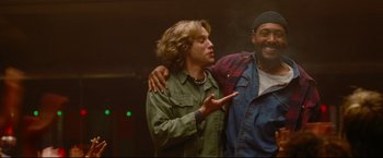 Movie still from “Rent” (2005), directed by Chris Columbus – Two men standing next to each other and one has his arm around the shoulder of another man; Medium shot, Low angle