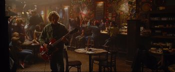 Movie still from “Rent” (2005), directed by Chris Columbus – A group of people sitting at a table in front of a guitar; Wide shot, Over the shoulder angle