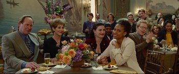 Movie still from “Rent” (2005), directed by Chris Columbus – A group of people sitting around a table with flowers; Medium shot, Over the shoulder angle