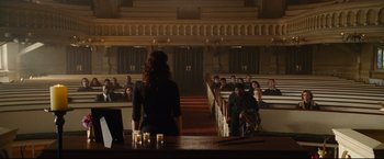 Movie still from “Rent” (2005), directed by Chris Columbus – A woman standing in front of a group of people in an auditorium; Wide shot, High angle