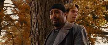 Movie still from “Rent” (2005), directed by Chris Columbus – A man with a beard and a hat is standing next to a tree; Close Up shot, Over the shoulder angle
