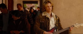 Movie still from “Rent” (2005), directed by Chris Columbus – A man holding a guitar while standing next to a wall; Medium shot, Over the shoulder angle