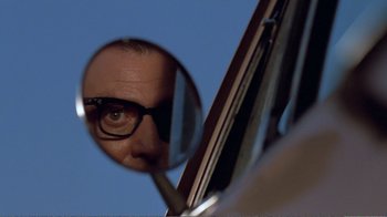 Movie still from “Repo Man” (1984), directed by Alex Cox – A man with glasses looking into a mirror; Extreme Close Up shot, Low angle