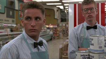 Movie still from “Repo Man” (1984), directed by Alex Cox – A man with a bow tie standing next to another man in a grocery store; Close Up shot, Low angle