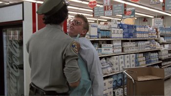 Movie still from “Repo Man” (1984), directed by Alex Cox – A man is being restrained by a police officer in a department store; Medium shot, Over the shoulder angle