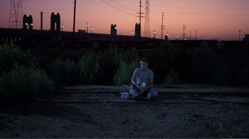 Movie still from “Repo Man” (1984), directed by Alex Cox – A man sitting on the side of a road at night; Wide shot, High angle