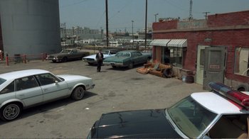 Movie still from “Repo Man” (1984), directed by Alex Cox – A man standing in a parking lot next to parked cars; Extreme Wide shot, High angle