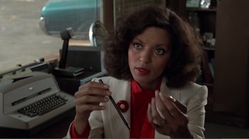 Movie still from “Repo Man” (1984), directed by Alex Cox – A woman in a white jacket holding a pen; Close Up shot, Over the shoulder angle