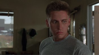 Movie still from “Repo Man” (1984), directed by Alex Cox – A young man in a gray t - shirt stares at the camera; Close Up shot, Low angle