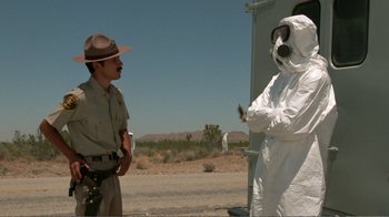 Movie still from “Repo Man” (1984), directed by Alex Cox – A man in a hazmat suit talking to a man in a hat; Medium shot, Over the shoulder angle