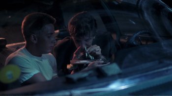 Movie still from “Repo Man” (1984), directed by Alex Cox – Two people sitting in a car looking at their cell phones; Medium shot, Low angle