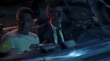 Movie still from “Repo Man” (1984), directed by Alex Cox – A man sitting in a car next to another man; Medium shot, High angle