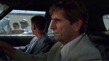 Movie still from “Repo Man” (1984), directed by Alex Cox – A man in a suit sitting in the back of a car; Close Up shot, Over the shoulder angle