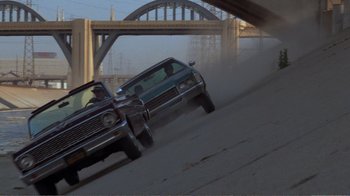 Movie still from “Repo Man” (1984), directed by Alex Cox – A couple of cars driving down a street; Wide shot, Low angle