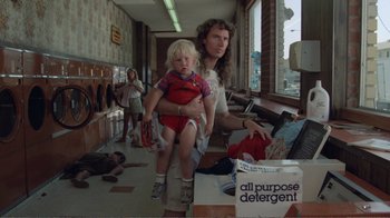 Movie still from “Repo Man” (1984), directed by Alex Cox – A woman holding a child in a laundry room; Medium shot, Low angle