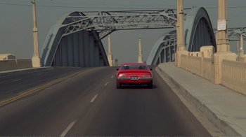 Movie still from “Repo Man” (1984), directed by Alex Cox – A red car driving on a road under a bridge; Extreme Wide shot, High angle