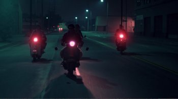 Movie still from “Repo Man” (1984), directed by Alex Cox – A group of people riding motorcycles down a street at night; Wide shot, Low angle