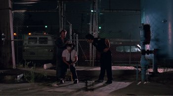 Movie still from “Repo Man” (1984), directed by Alex Cox – A group of men standing next to each other on a field; Wide shot, Over the shoulder angle