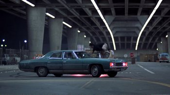 Movie still from “Repo Man” (1984), directed by Alex Cox – A man riding a bike on the hood of a car; Wide shot, Low angle