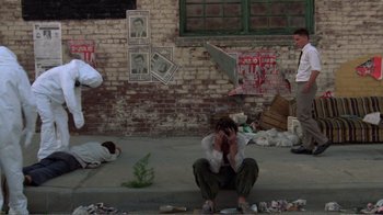 Movie still from “Repo Man” (1984), directed by Alex Cox – A man sitting on the ground in front of a brick wall; Wide shot, High angle