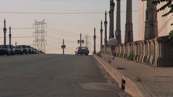 Movie still from “Repo Man” (1984), directed by Alex Cox – A man running down the side of a road; Extreme Wide shot, High angle