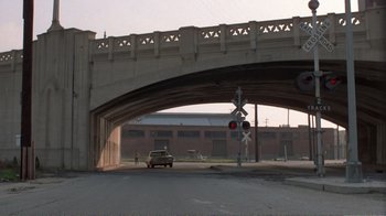 Movie still from “Repo Man” (1984), directed by Alex Cox – A car driving under an overpass near a train station; Extreme Wide shot, High angle