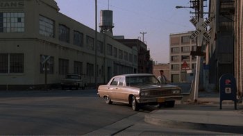 Movie still from “Repo Man” (1984), directed by Alex Cox – A man standing next to an old car on the side of the road; Wide shot, High angle