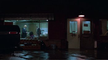 Movie still from “Repo Man” (1984), directed by Alex Cox – Two people are standing outside of a store at night; Extreme Wide shot, High angle