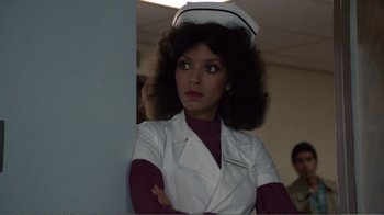 Movie still from “Repo Man” (1984), directed by Alex Cox – A woman in a nurse's uniform with her arms crossed looking at the camera; Close Up shot, Over the shoulder angle