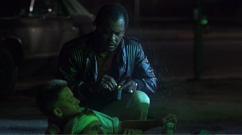 Movie still from “Repo Man” (1984), directed by Alex Cox – A man sitting on the ground next to a young boy; Medium shot, Low angle