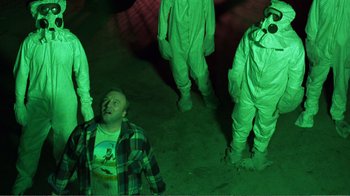 Movie still from “Repo Man” (1984), directed by Alex Cox – A group of people standing around a man in a green suit; Medium shot, Low angle